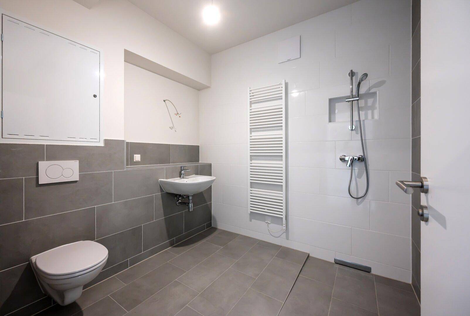 Modernes Badezimmer mit ebenerdiger Dusche, wandhängendem WC und Handtuchheizkörper.