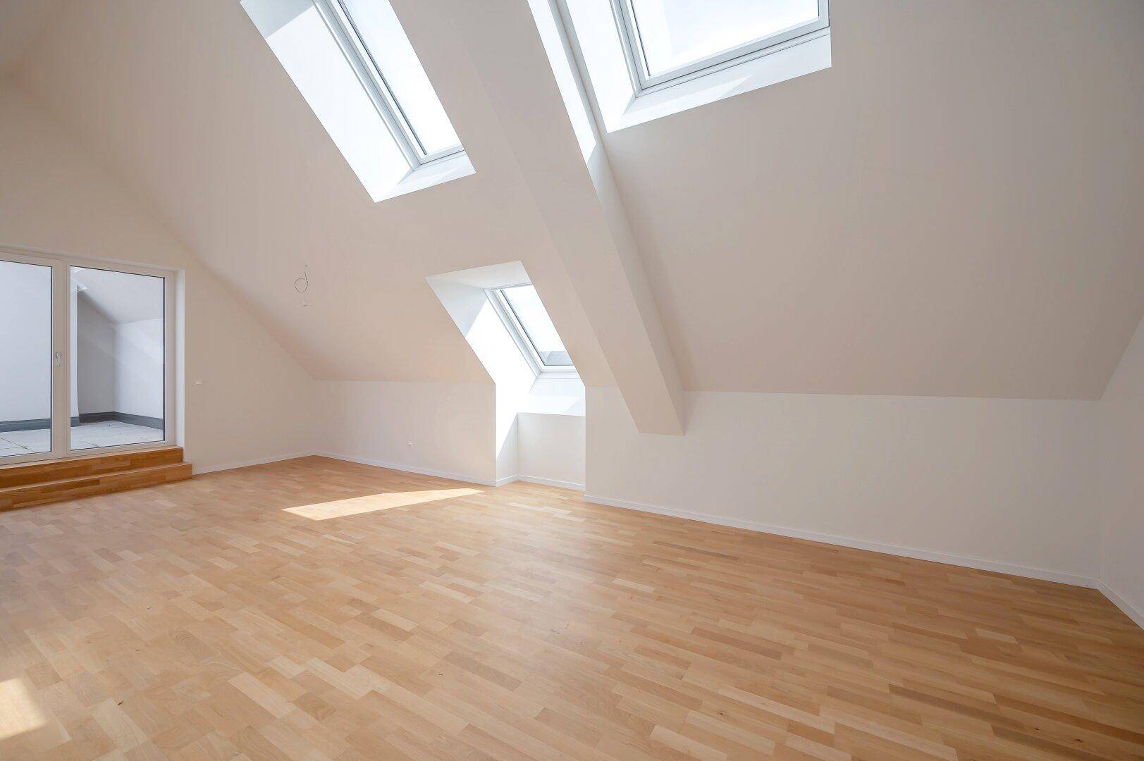 Lichtdurchfluteter Dachgeschossraum mit Holzparkett, hohen Decken und mehreren Dachfenstern.