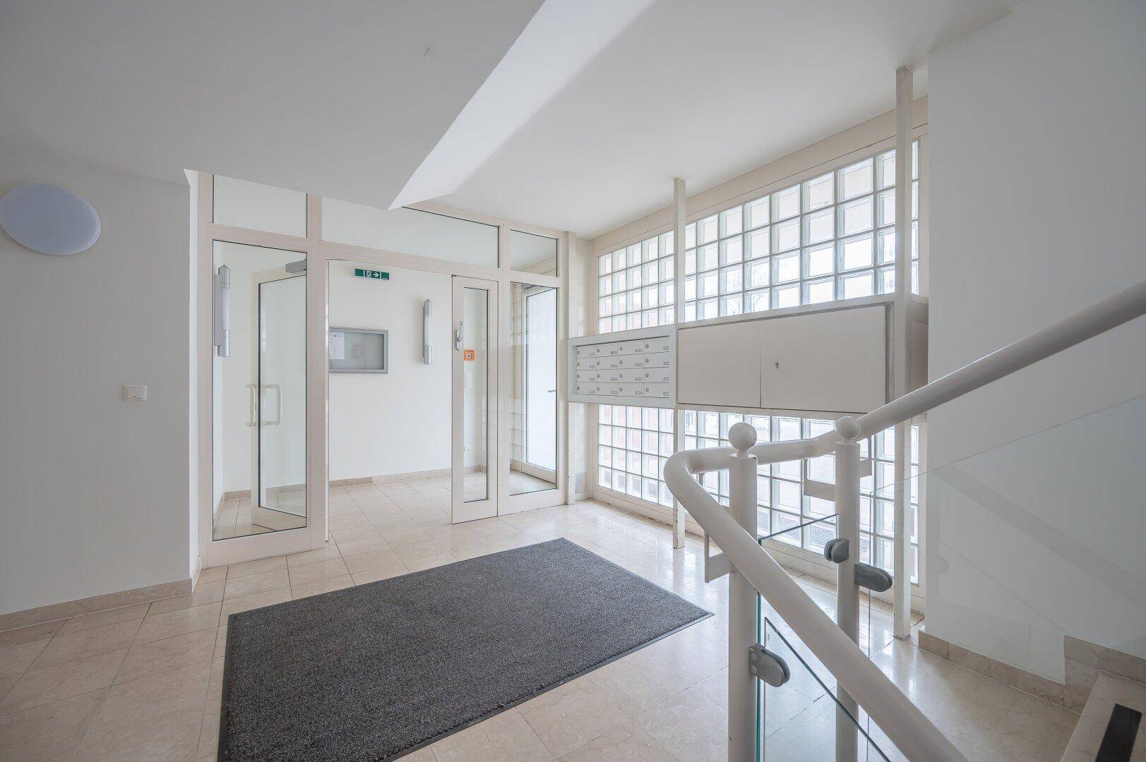 Heller Eingangsbereich mit Glasbausteinwand, Briefkästen und Zugang zum Treppenhaus.