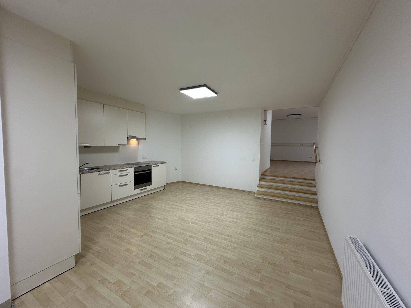 Heller Wohnbereich mit Küchenzeile, Laminatboden und Treppe, die in eine untere Etage führt.