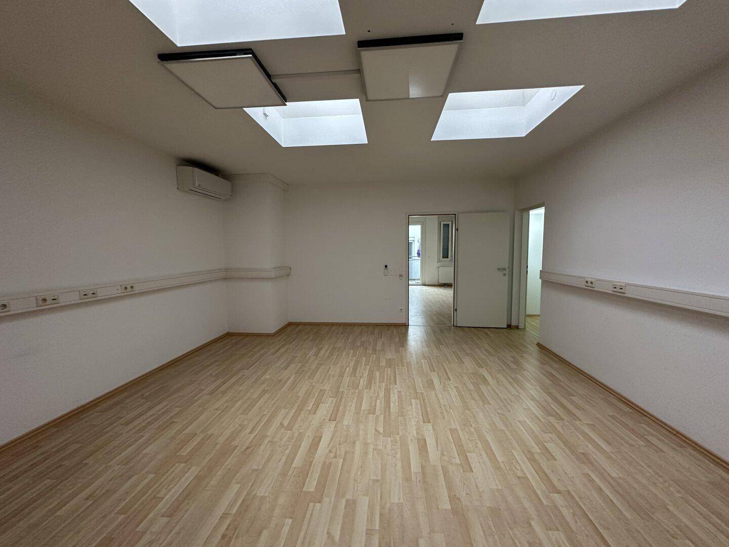 Heller Raum mit Laminatboden, Dachfenstern, Klimaanlage und Zugang zu weiteren Räumen.