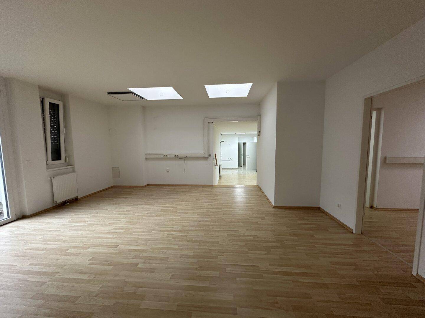 Geräumiger Raum mit Laminatboden, Dachfenstern und einem Fenster mit Rollladen.