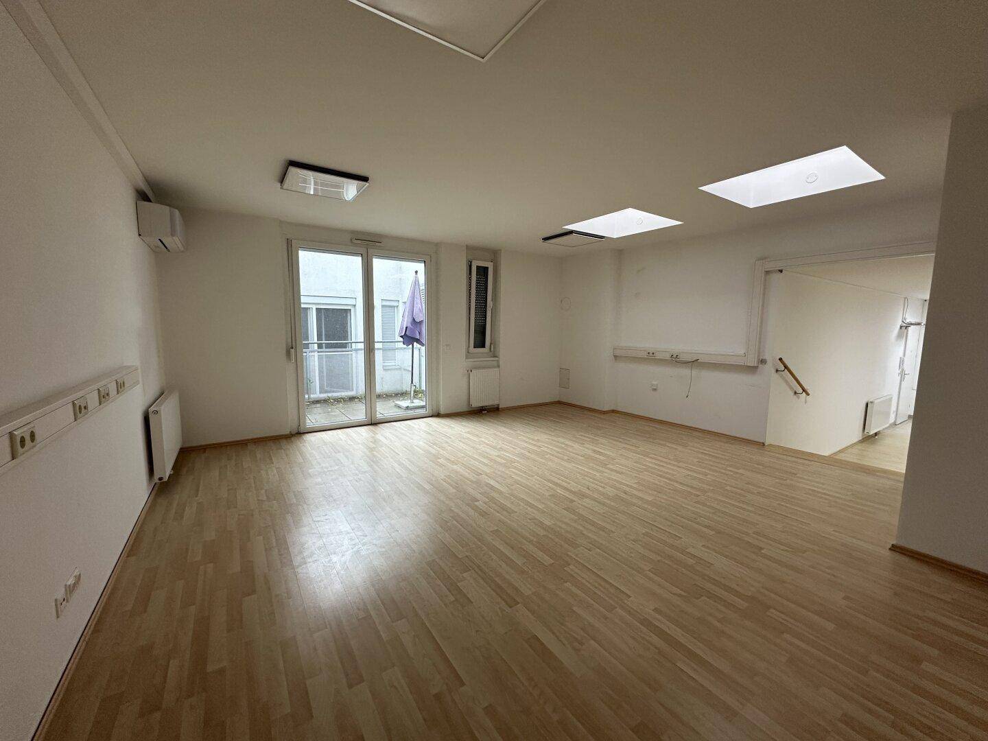 Heller Raum mit Laminatboden, Dachfenstern, Klimaanlage und Zugang zu einer Terrasse.