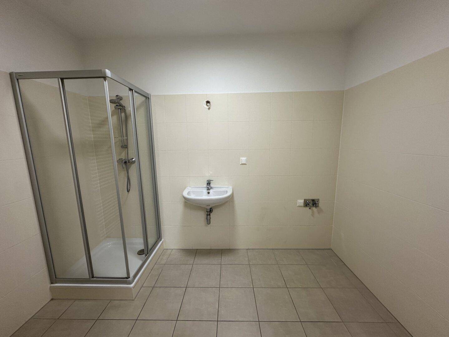 Helles Badezimmer mit beigefarbenen Fliesen, einer Duschkabine und einem Waschbecken.