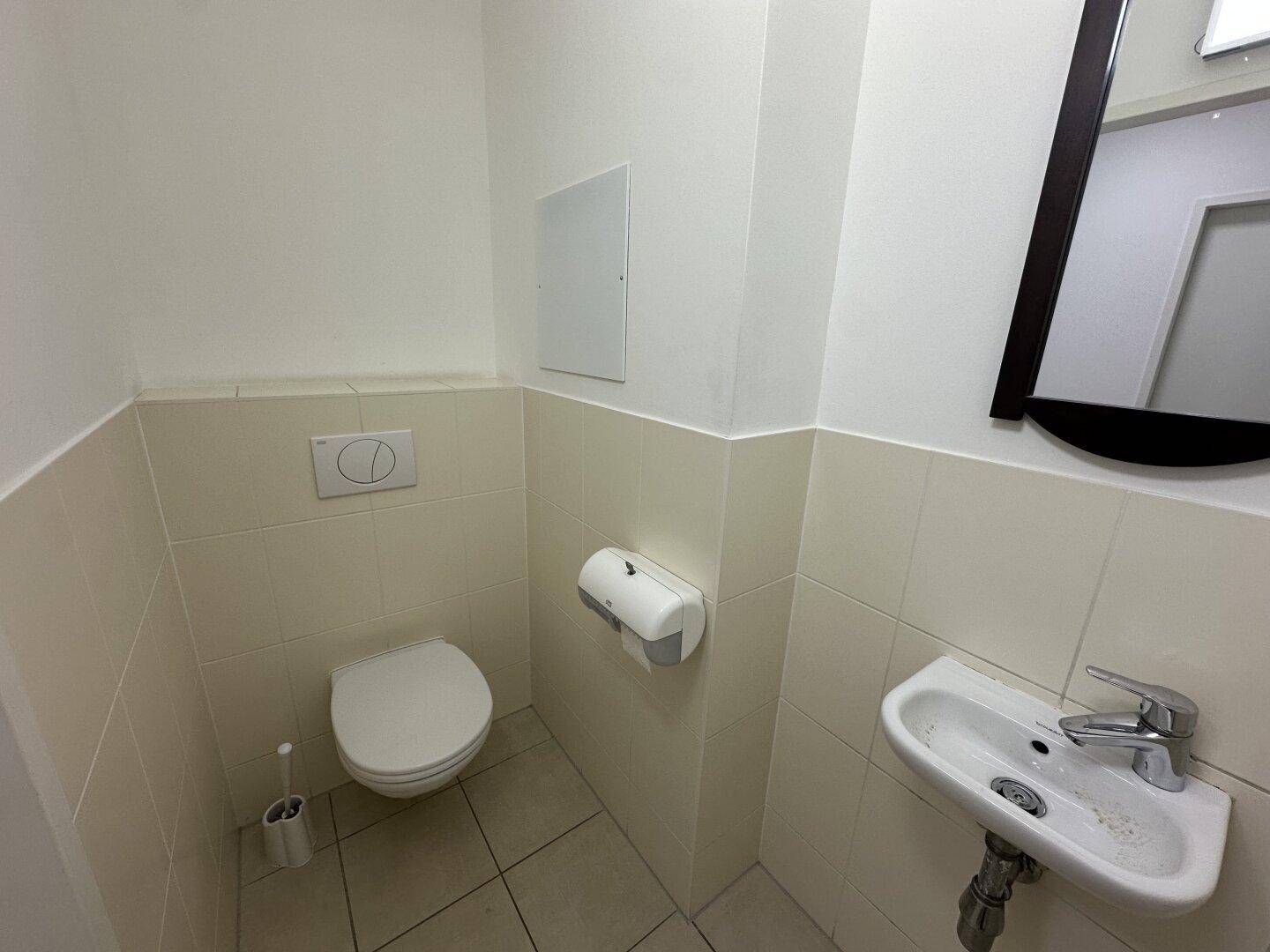 Kleines Gäste-WC mit wandhängender Toilette, kleinem Waschbecken und hellen Fliesen.