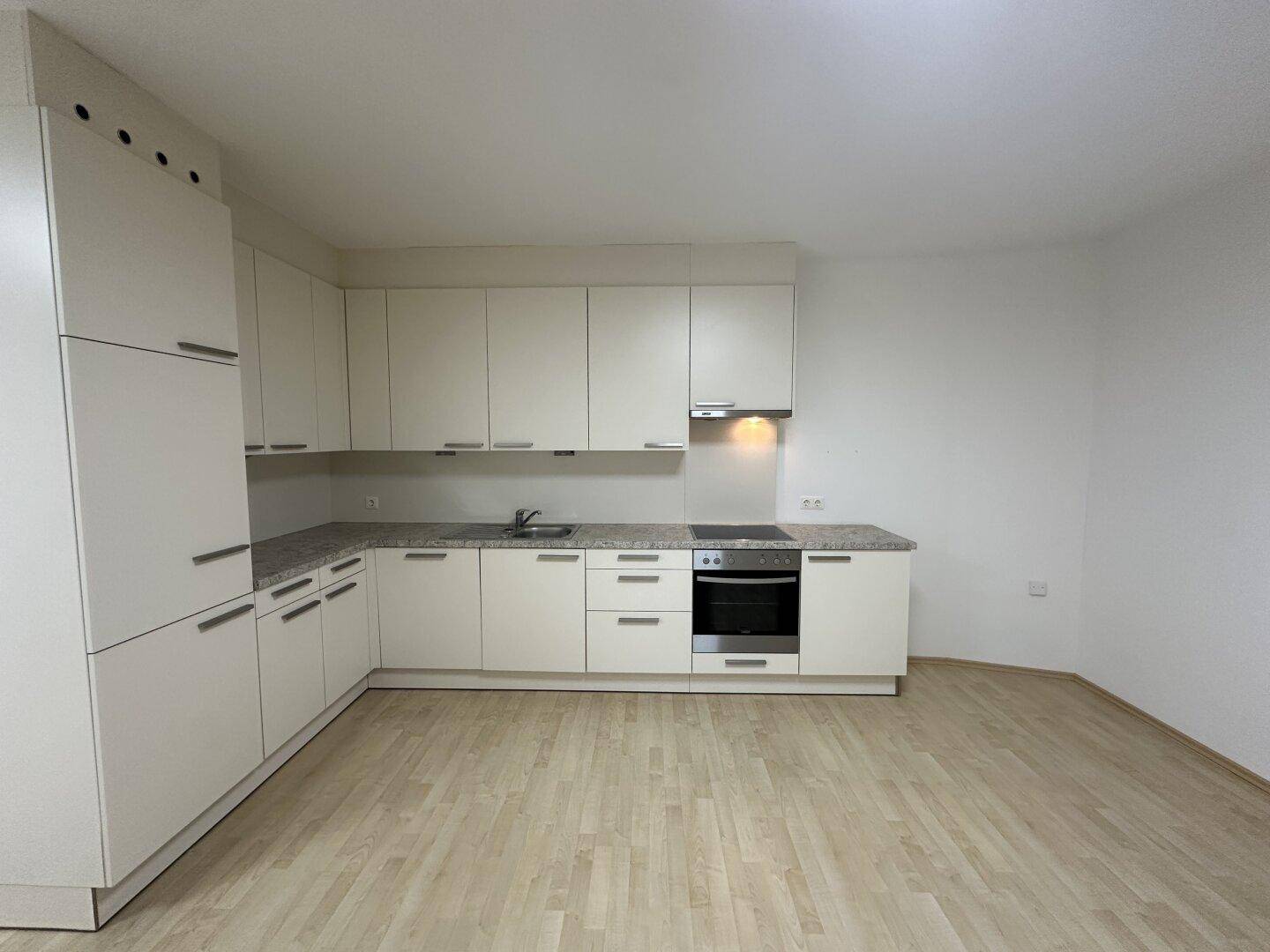 Moderne L-förmige Küche mit weißen Schränken, gesprenkelter Arbeitsplatte und integrierten Geräten.