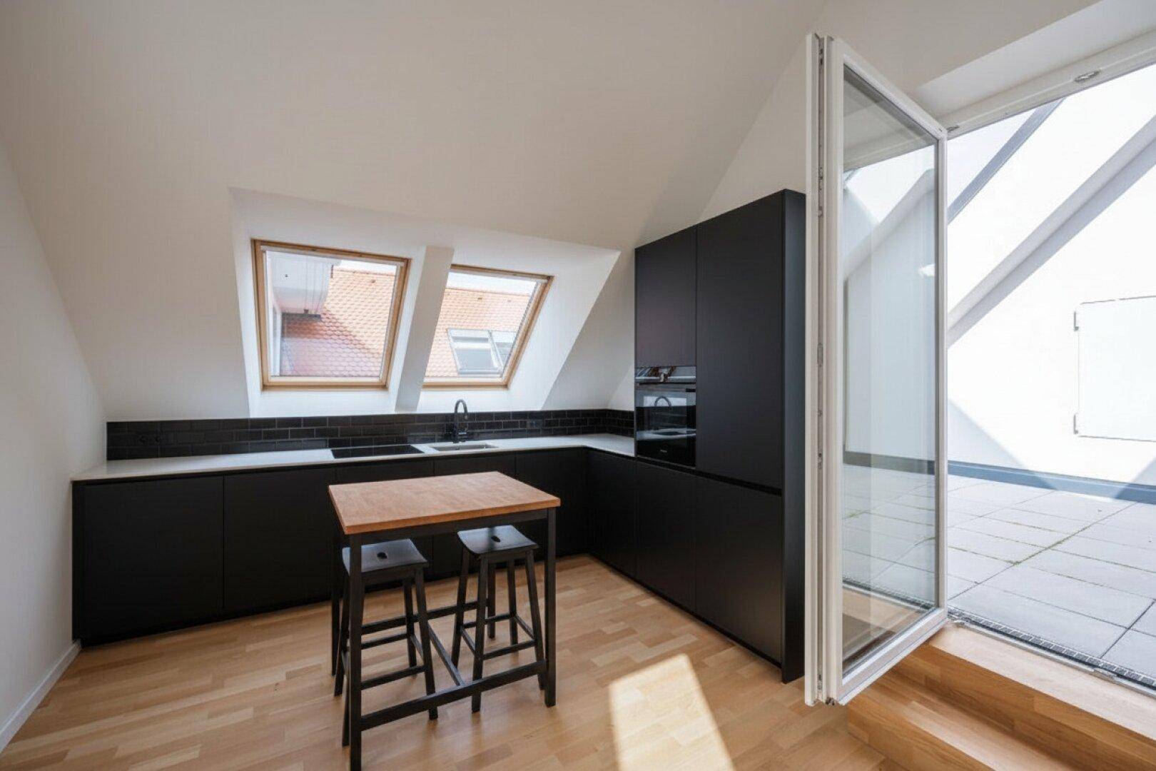 Moderne schwarze Küche im Dachgeschoss mit Kochinsel, Dachfenstern und Terrassenzugang.