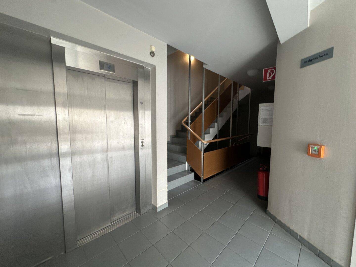 Eingangsbereich mit Aufzug, Treppenhaus und Fliesenboden, der einen modernen Eindruck vermittelt.