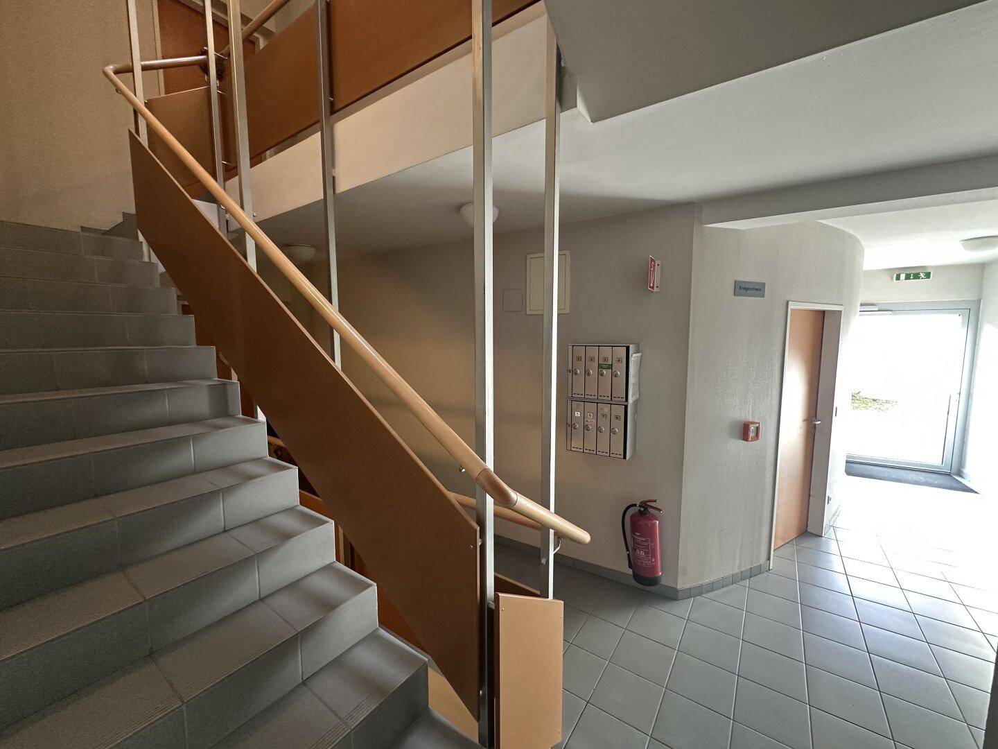 Modernes Treppenhaus mit Holzgeländer und grauen Stufen, das zu den oberen Etagen führt.