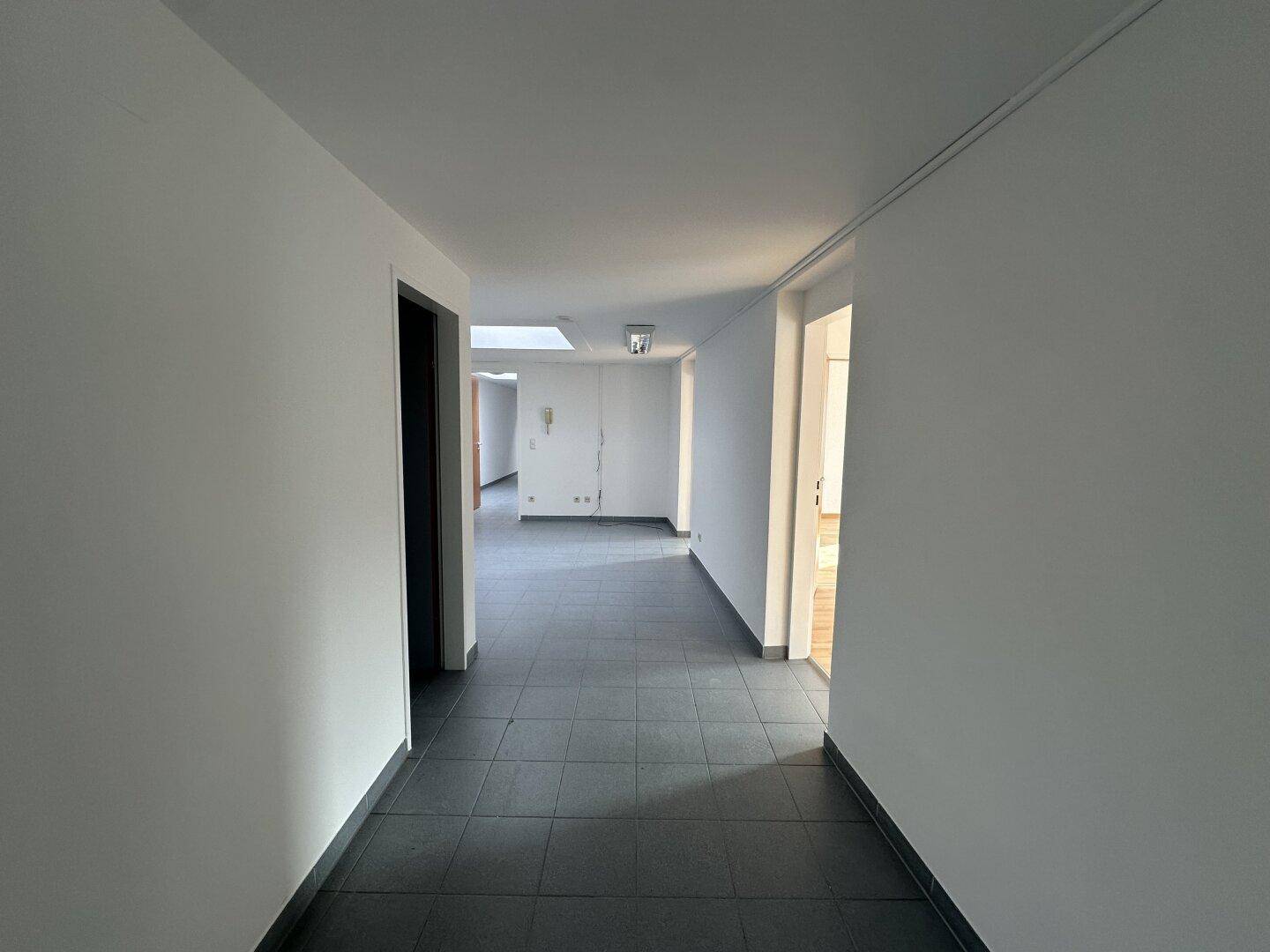 Langer, heller Flur mit grauen Fliesen und Oberlicht, der verschiedene Bereiche verbindet.