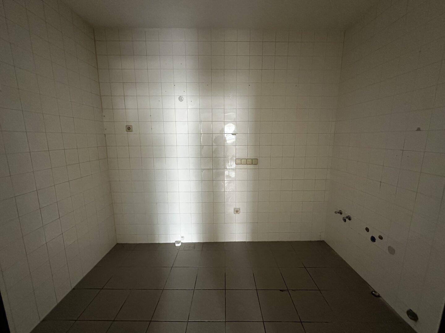 Kleiner Raum mit weißen Wandfliesen und dunklem Fliesenboden, ideal als Abstellraum oder Vorbereitungsküche.