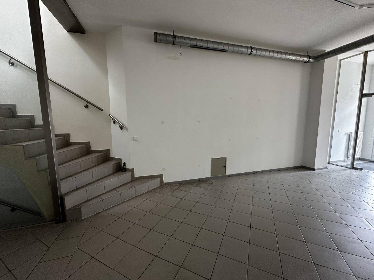 Geräumiger Gewerberaum mit Fliesenboden und einer Treppe, die in die obere Etage führt.
