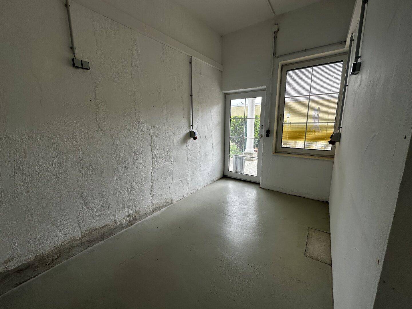 Abstellraum mit Fenster und Tür zum Außenbereich, Betonboden und einfachen Wänden.