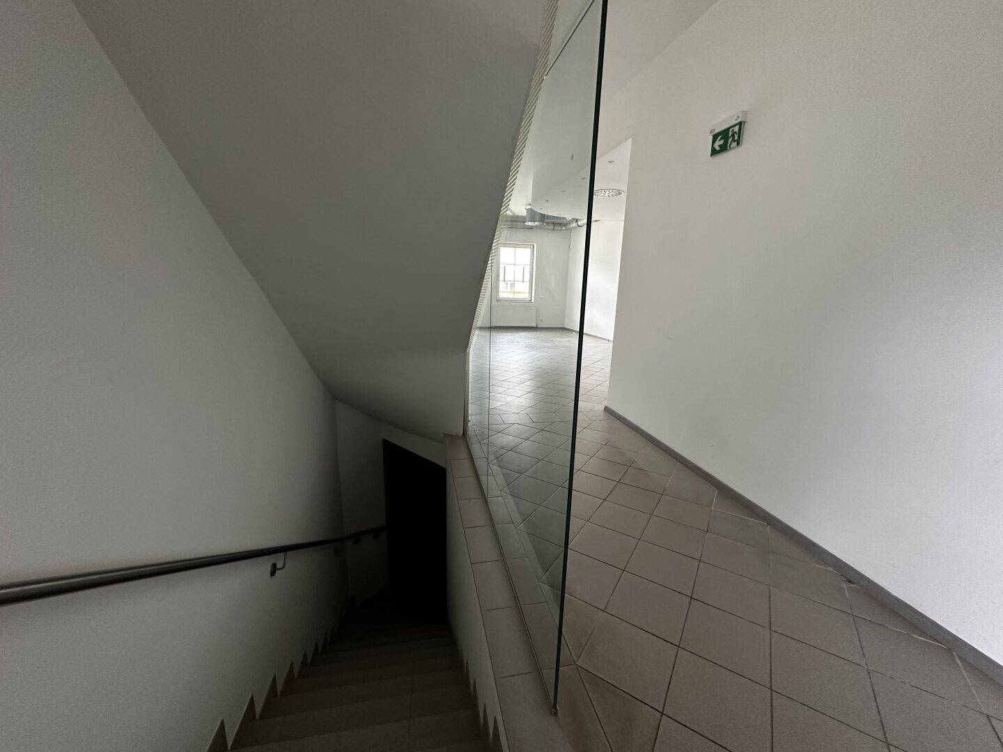 Treppenhaus mit Glasgeländer und Handlauf, das in die untere Etage führt.