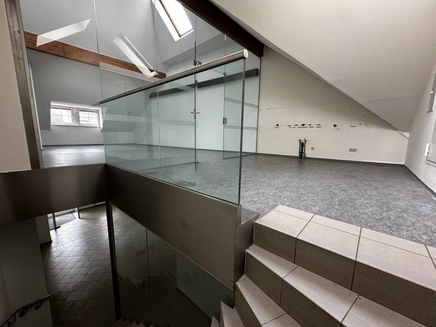 Offener Raum im Obergeschoss mit Dachschrägen, sichtbaren Holzbalken und Glasgeländer.