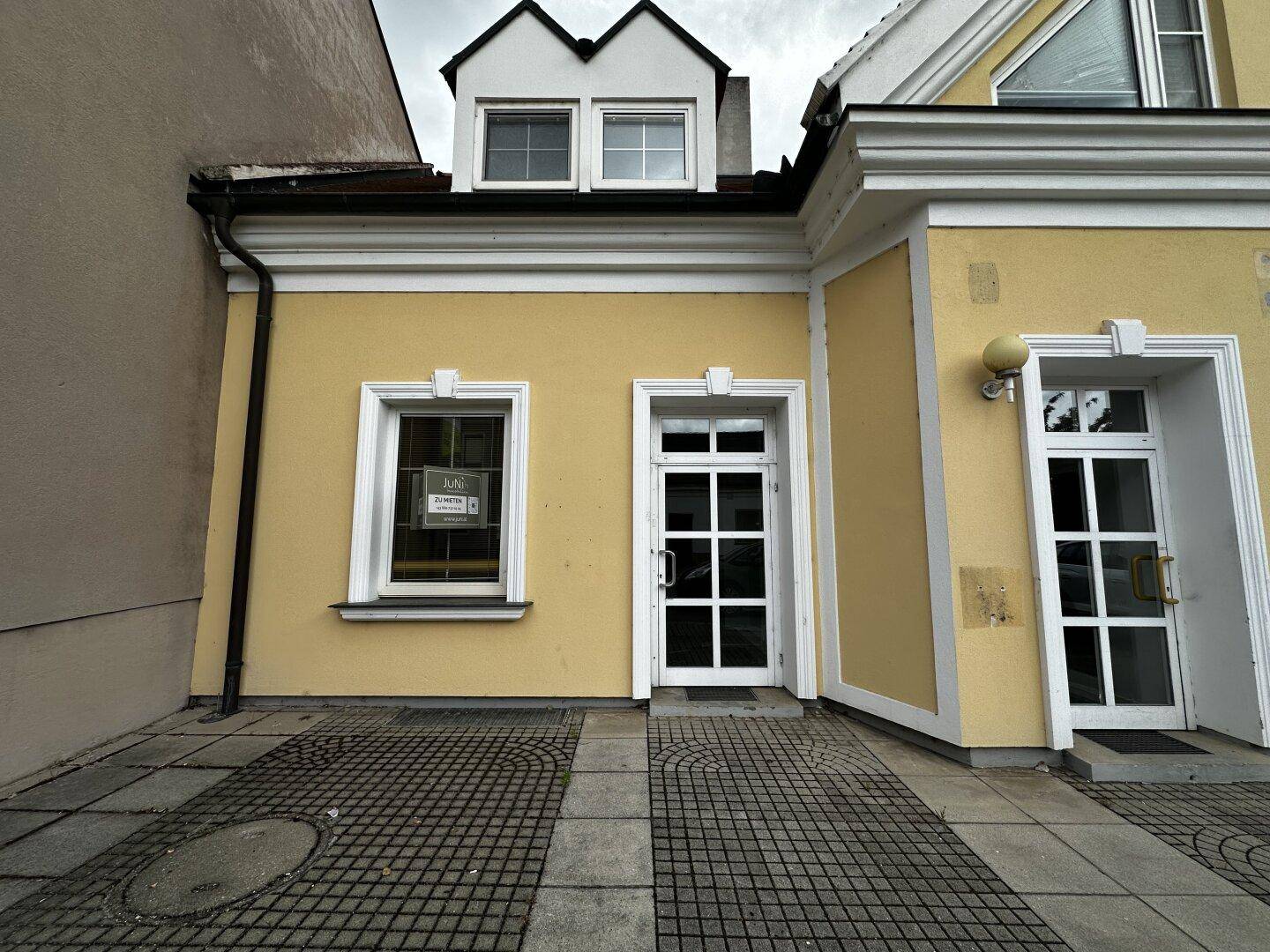 Gelbe Fassade eines Gebäudes mit weißen Fenstern und Türen, sowie einem Dachgiebel.