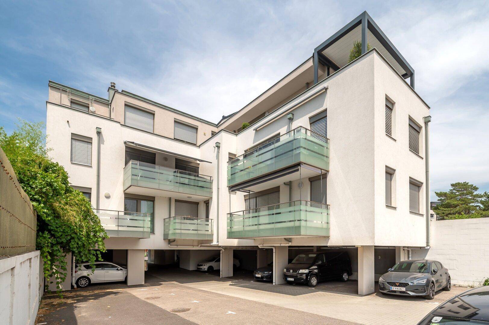 Modernes Mehrfamilienhaus mit Balkonen und überdachten Stellplätzen im Erdgeschoss.