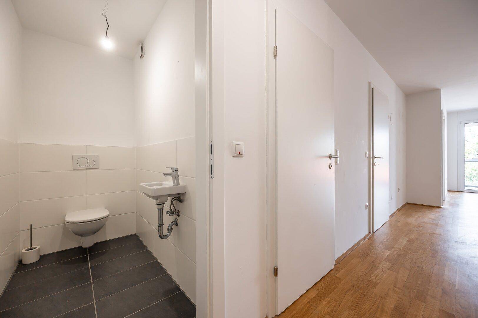 Modernes Gäste-WC mit dunklen Fliesen, wandhängendem WC und kleinem Waschbecken.