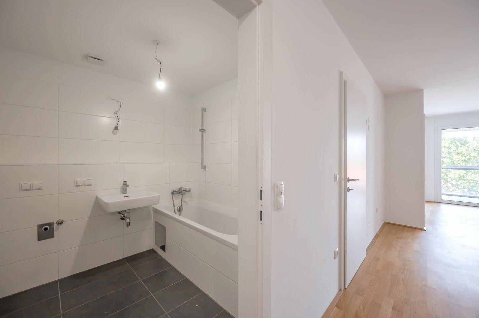 Modernes Badezimmer mit Badewanne, Waschbecken und dunklen Bodenfliesen, hell gefliesten Wänden.