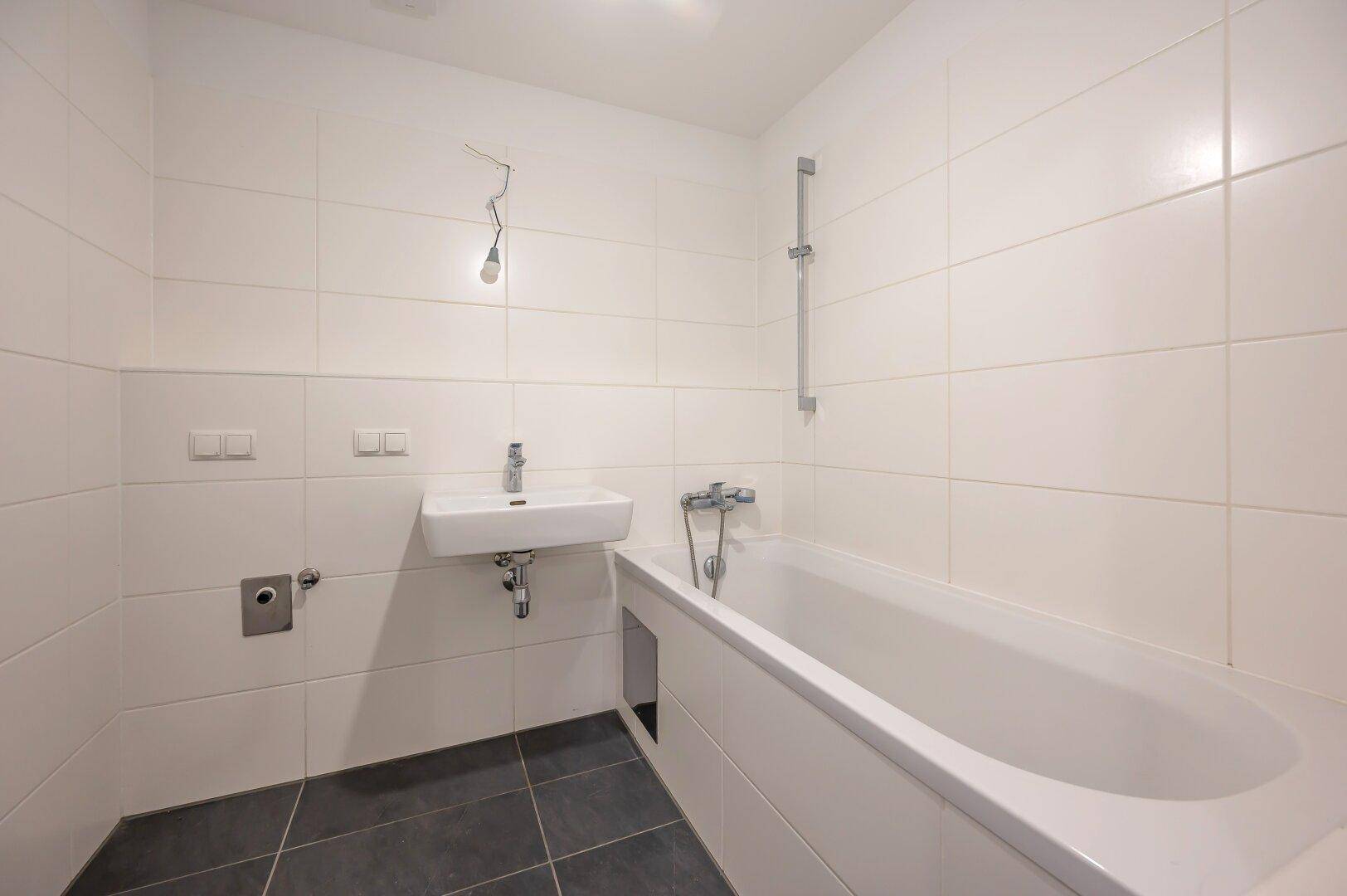 Detailansicht des Badezimmers mit Badewanne, Duscharmatur und modernem Waschbecken.