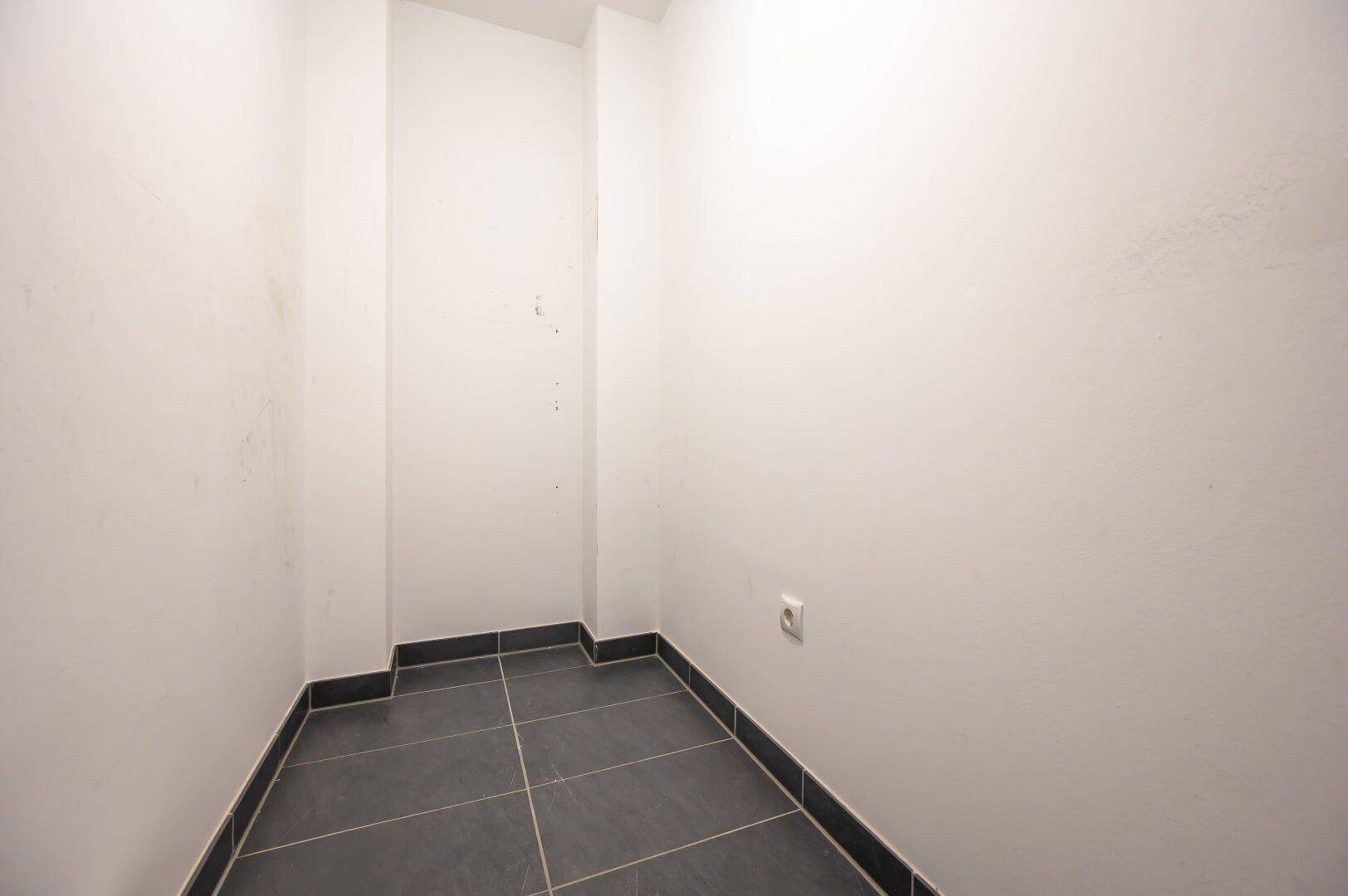 Kleiner Abstellraum mit dunklen Bodenfliesen und weißen Wänden, ideal für zusätzlichen Stauraum.