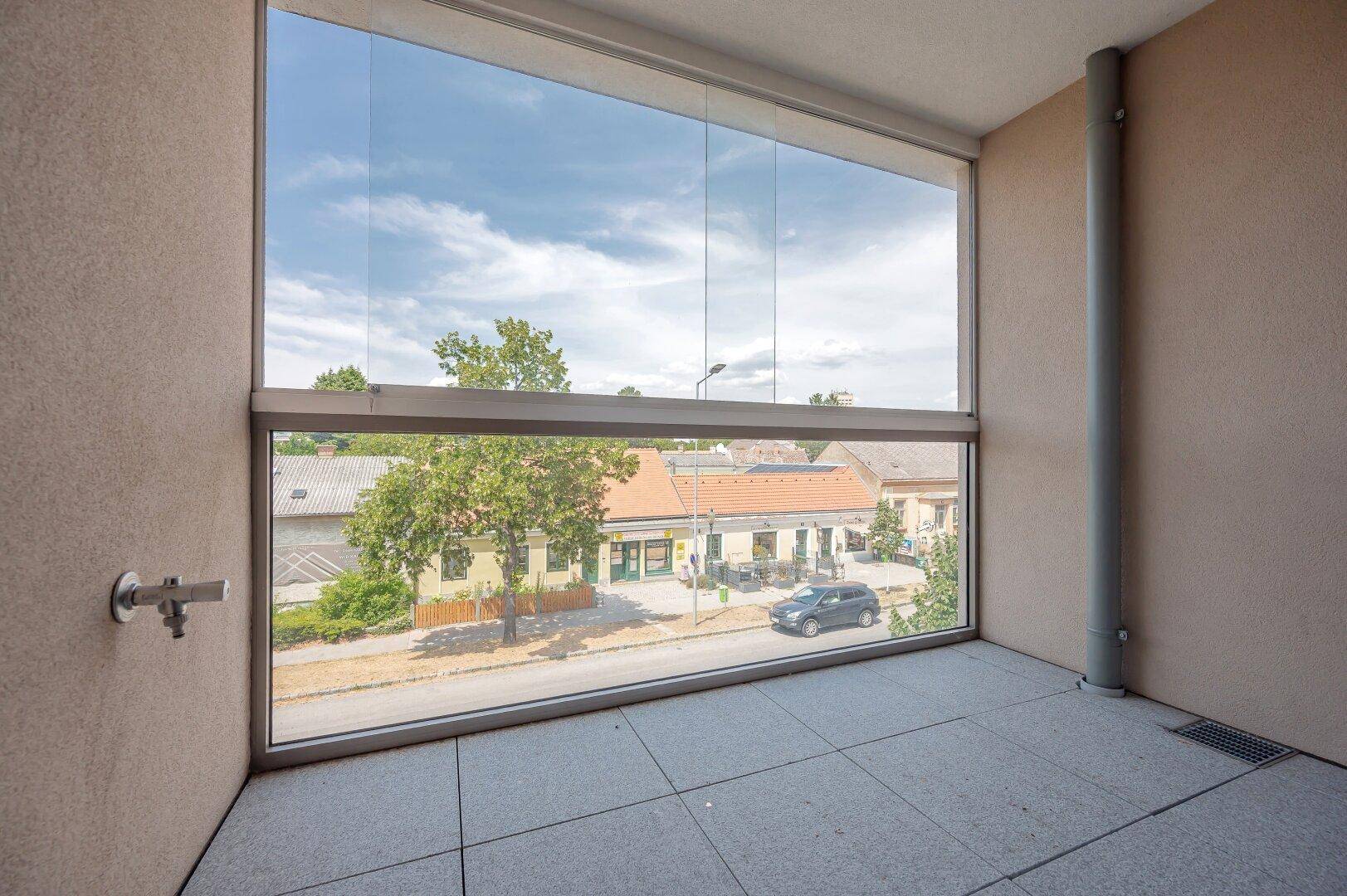 Verglaste Loggia mit Fliesenboden und Blick auf die Straße und umliegende Gebäude.