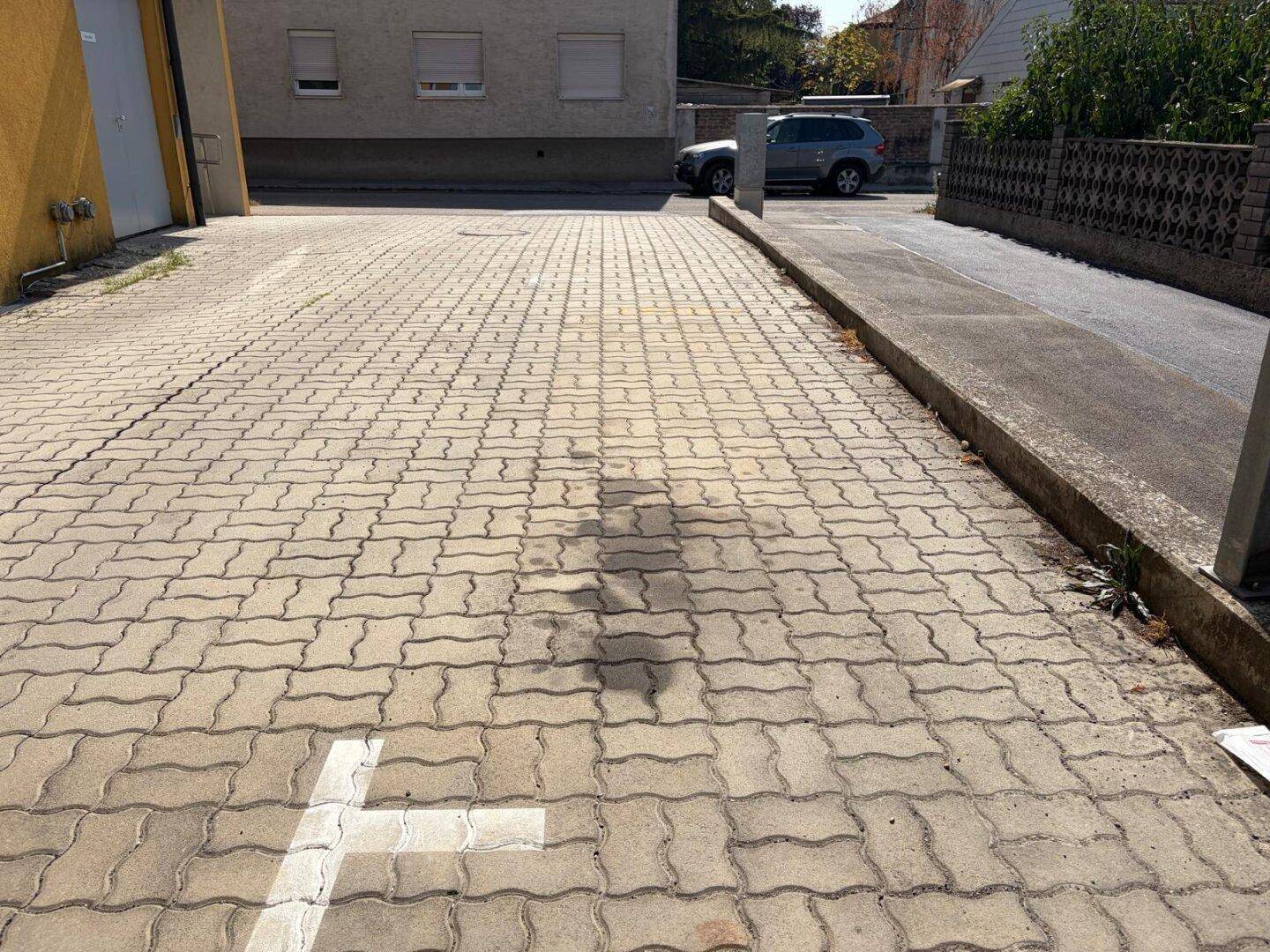 Gepflasterte Zufahrt mit Carport-Struktur auf der rechten Seite und Blick auf die Straße.