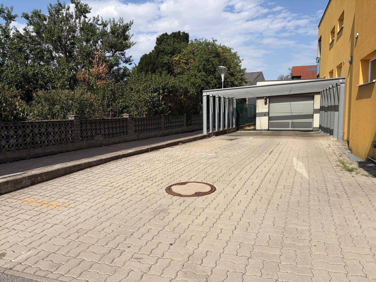 Gesamtansicht des Außenbereichs mit Carport, Garage, gelbem Gebäude und umgebender Bepflanzung.