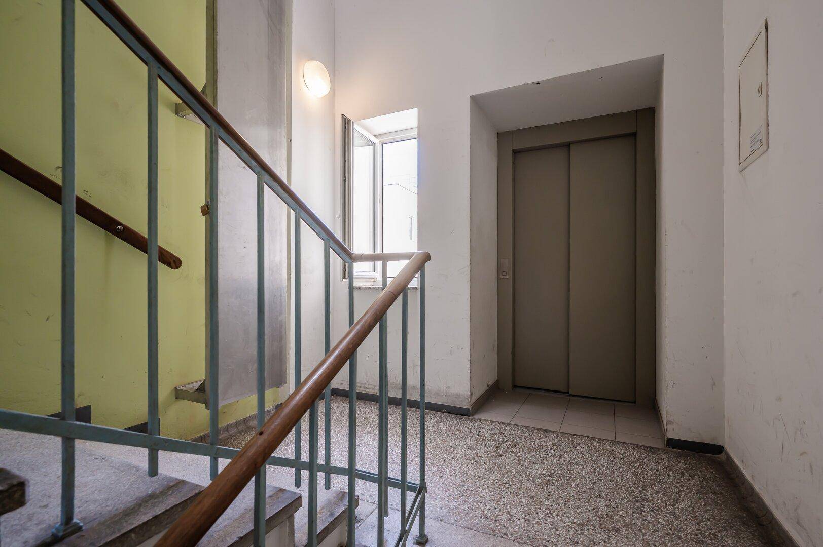 Treppenhaus mit Aufzug und einem kleinen Fenster, das für natürliche Belichtung sorgt.