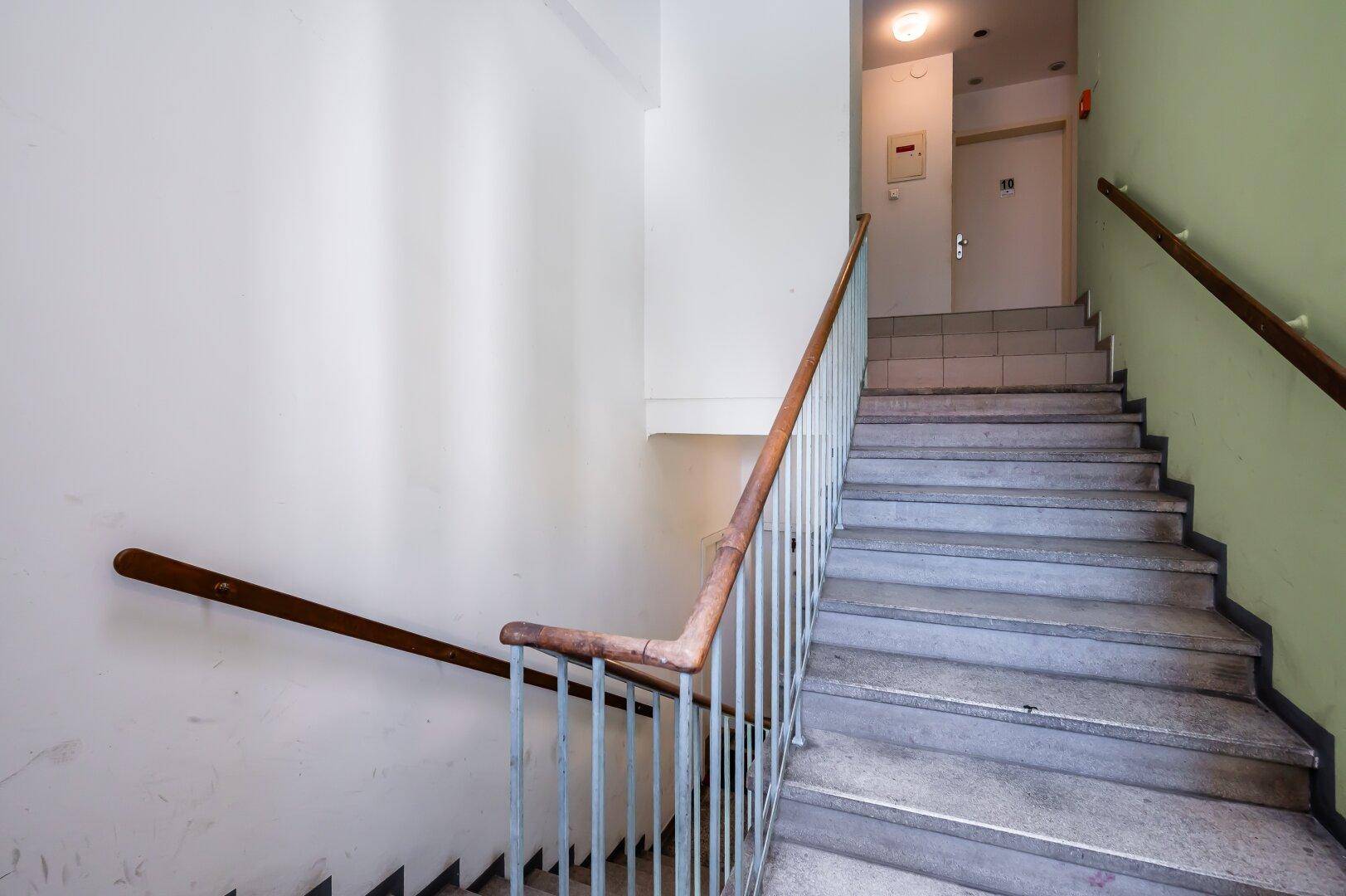 Helles Treppenhaus mit gefliestem Podest und robustem Metallgeländer in einem Mehrfamilienhaus.