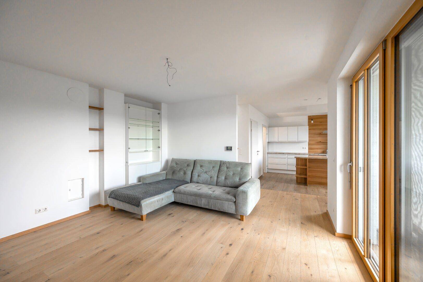 Geräumiges Wohnzimmer mit Sofa, Holzboden und Zugang zur offenen Küche.