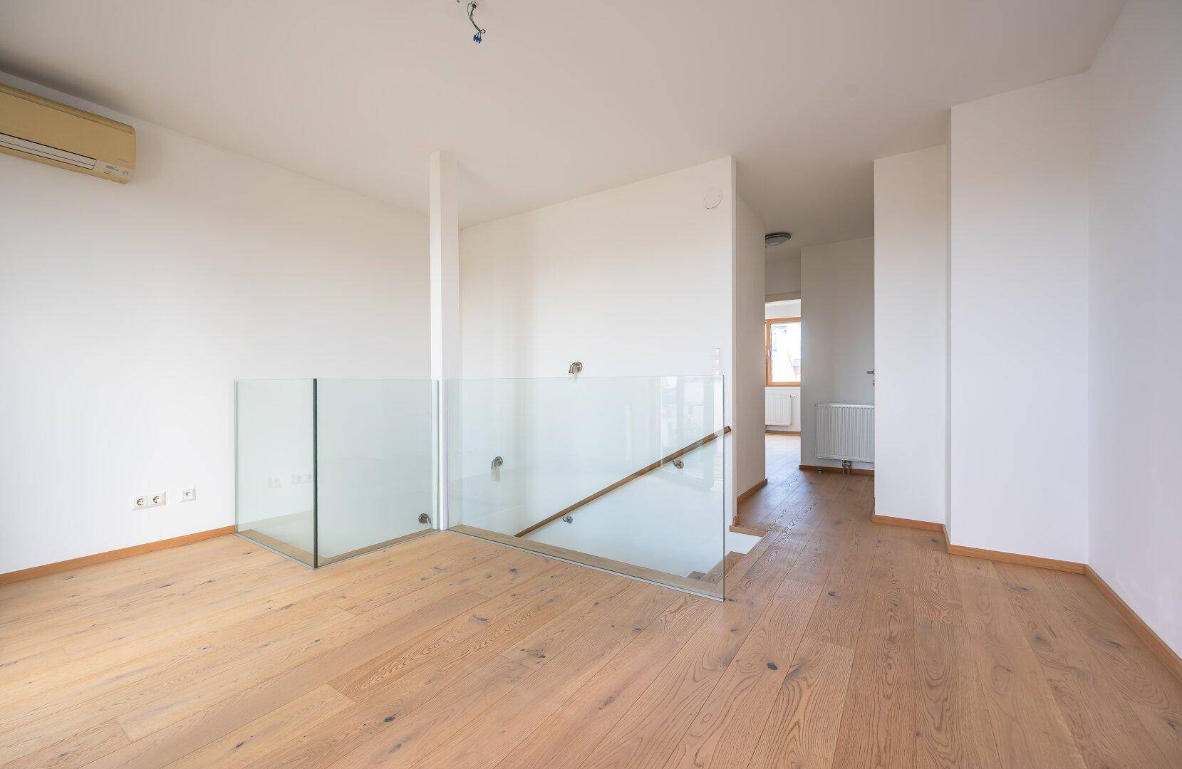 Heller Flur im Obergeschoss mit modernem Glasgeländer und Holzboden.