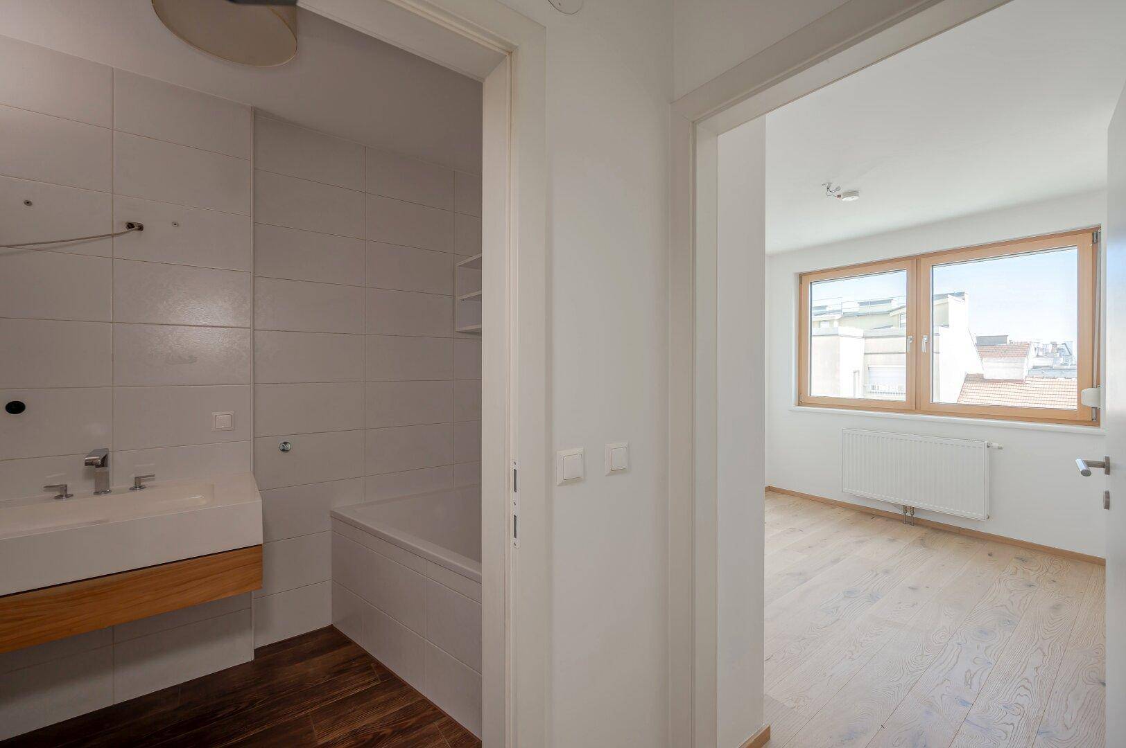 Schlafzimmer mit Holzboden und Blick in ein angrenzendes Badezimmer.