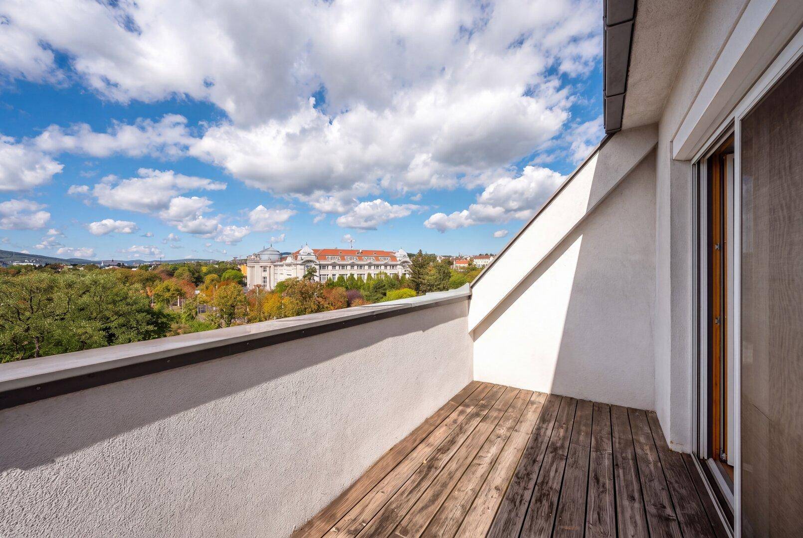 Sonniger Balkon mit Holzbelag und weitem Blick über die Stadt und grüne Umgebung.