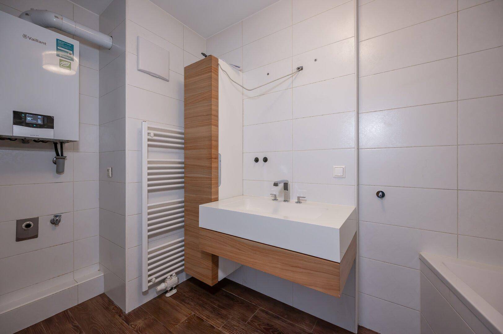 Badezimmer mit modernem Waschbecken, Handtuchheizkörper und Warmwasserboiler.