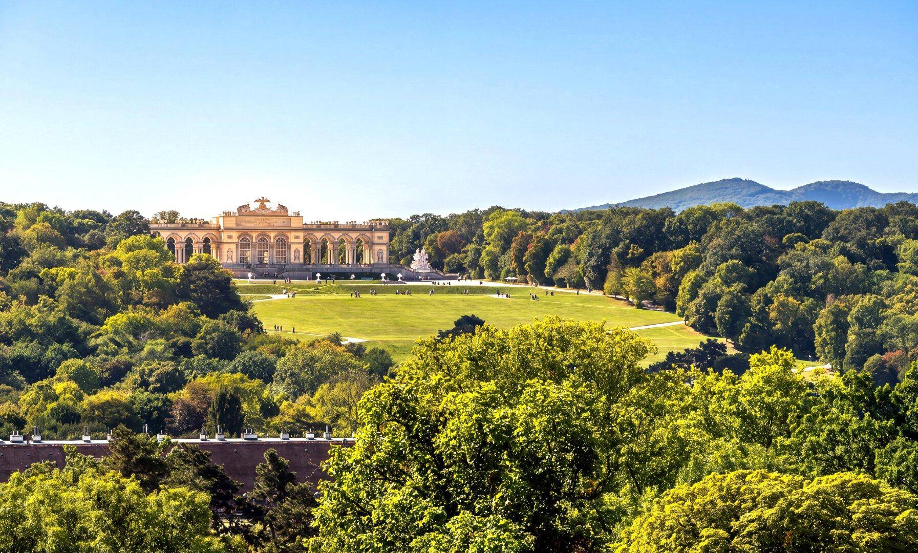 Weitläufiger Blick über eine grüne Parklandschaft mit historischem Schloss im Hintergrund.