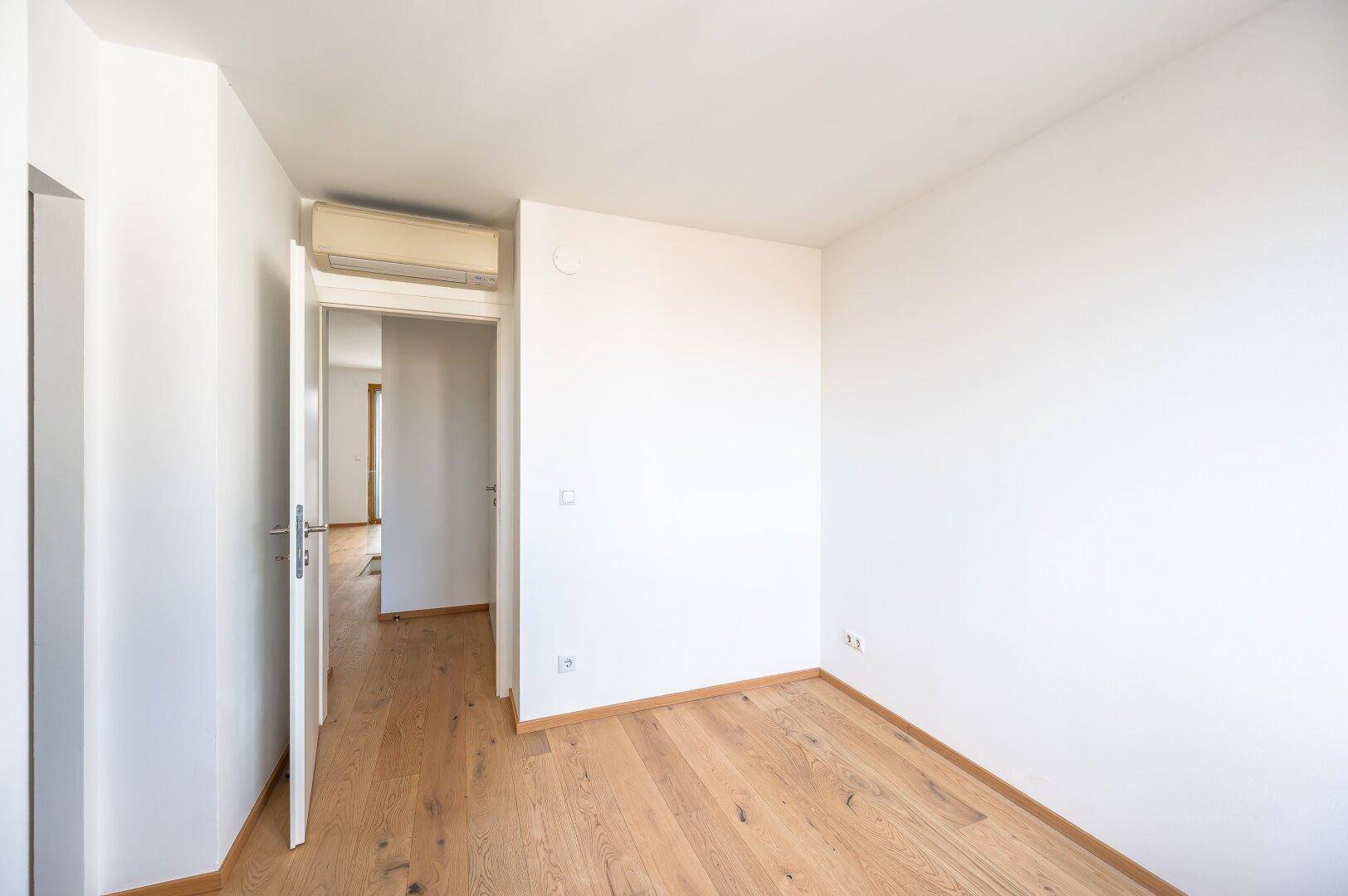 Helles, leeres Zimmer mit Holzboden und Klimaanlage, ideal als Schlaf- oder Arbeitszimmer.