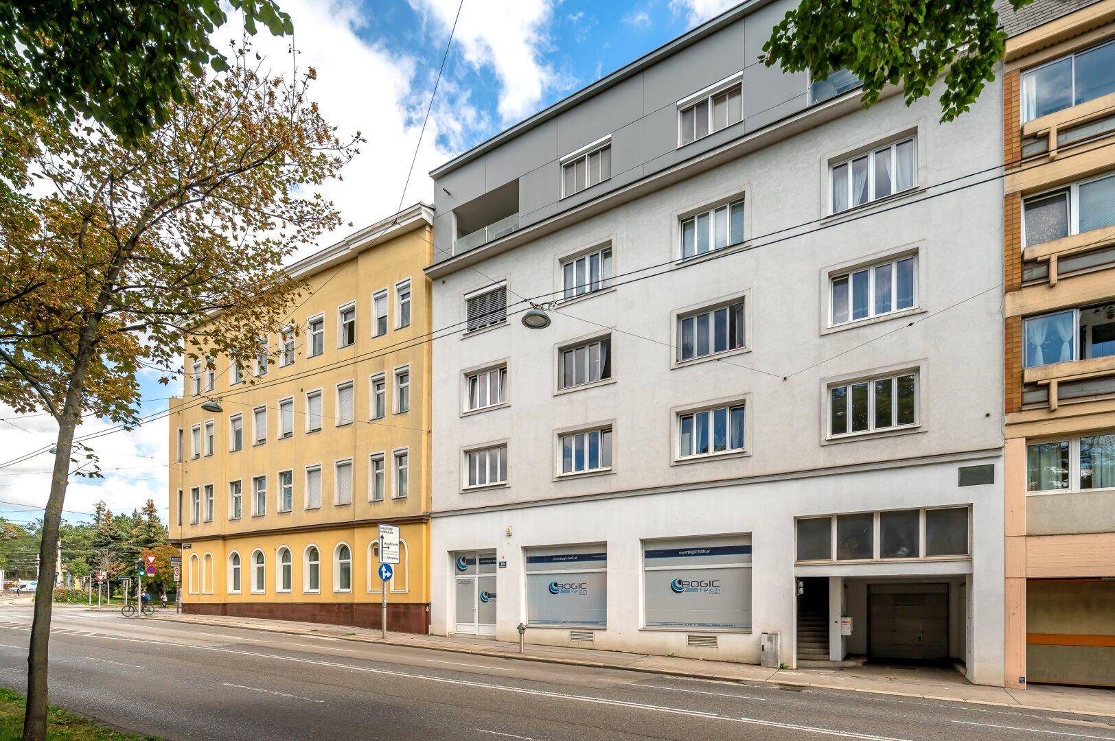 Moderne Gebäudefassade mit großen Fenstern und Geschäften im Erdgeschoss an einer belebten Straße.