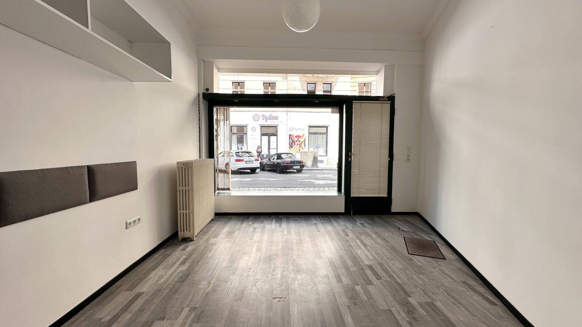 Heller Geschäftsraum mit breiter Fensterfront zur Straße und einem klassischen Heizkörper unter dem Fenster.