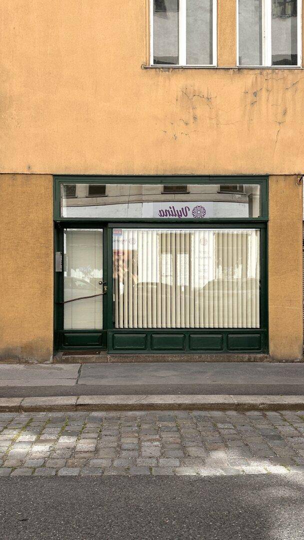 Fassade eines Geschäftsgebäudes mit großer Schaufensterfront und gepflastertem Gehweg davor.