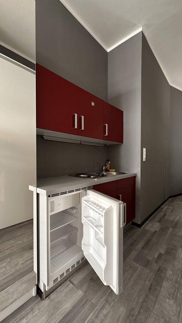 Küchenzeile mit roten Schränken und integriertem, geöffnetem Kühlschrank, ideal für kleine Räume.