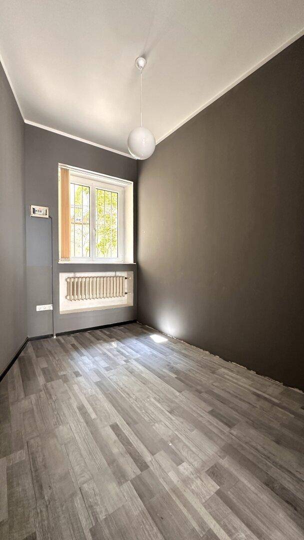 Ruhiger Raum mit Fenster, grauem Anstrich und Laminatboden, bietet angenehmes Tageslicht.