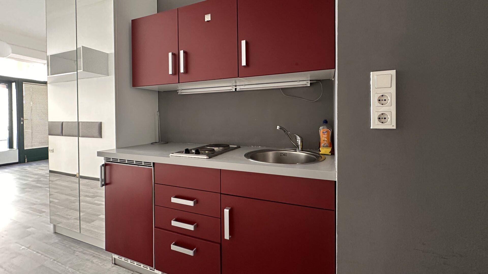Kompakte Küchenzeile mit roten Schränken, Spüle und zwei Kochfeldern in modernem Design.