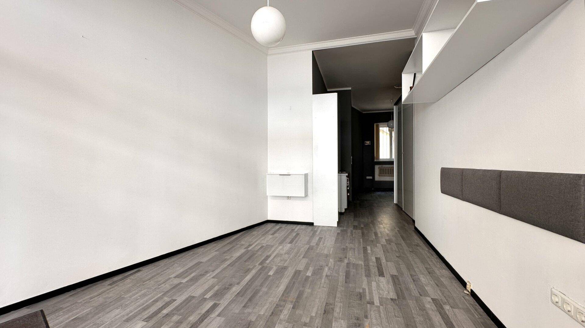 Geräumiger Innenraum mit hellem Laminatboden, weißen Wänden und Zugang zu weiteren Bereichen.