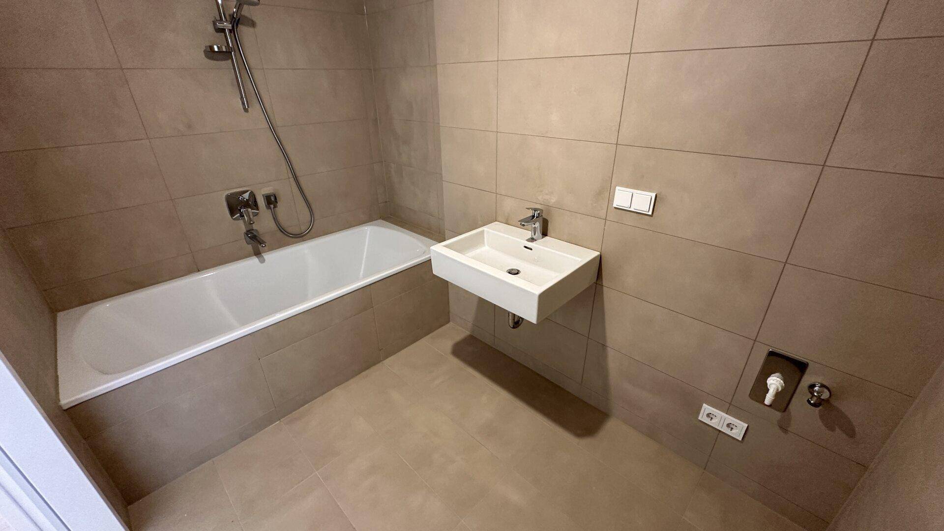 Modernes Badezimmer mit Badewanne, Wandwaschbecken und beigefarbenen Fliesen.