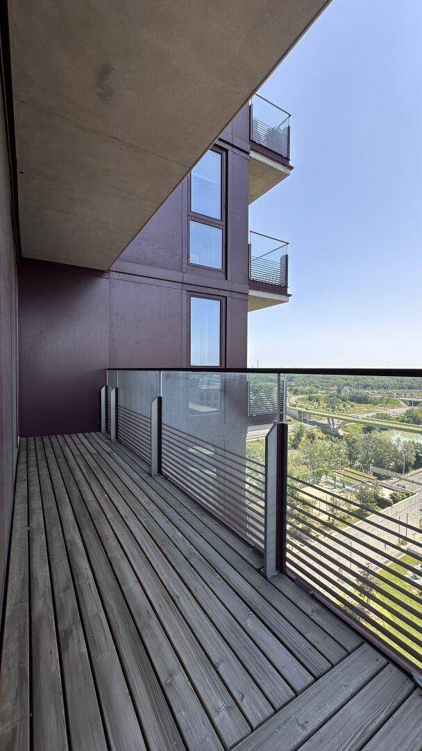 Geräumiger Balkon mit Holzbelag und Glasgeländer, bietet einen weiten Blick in die Ferne.