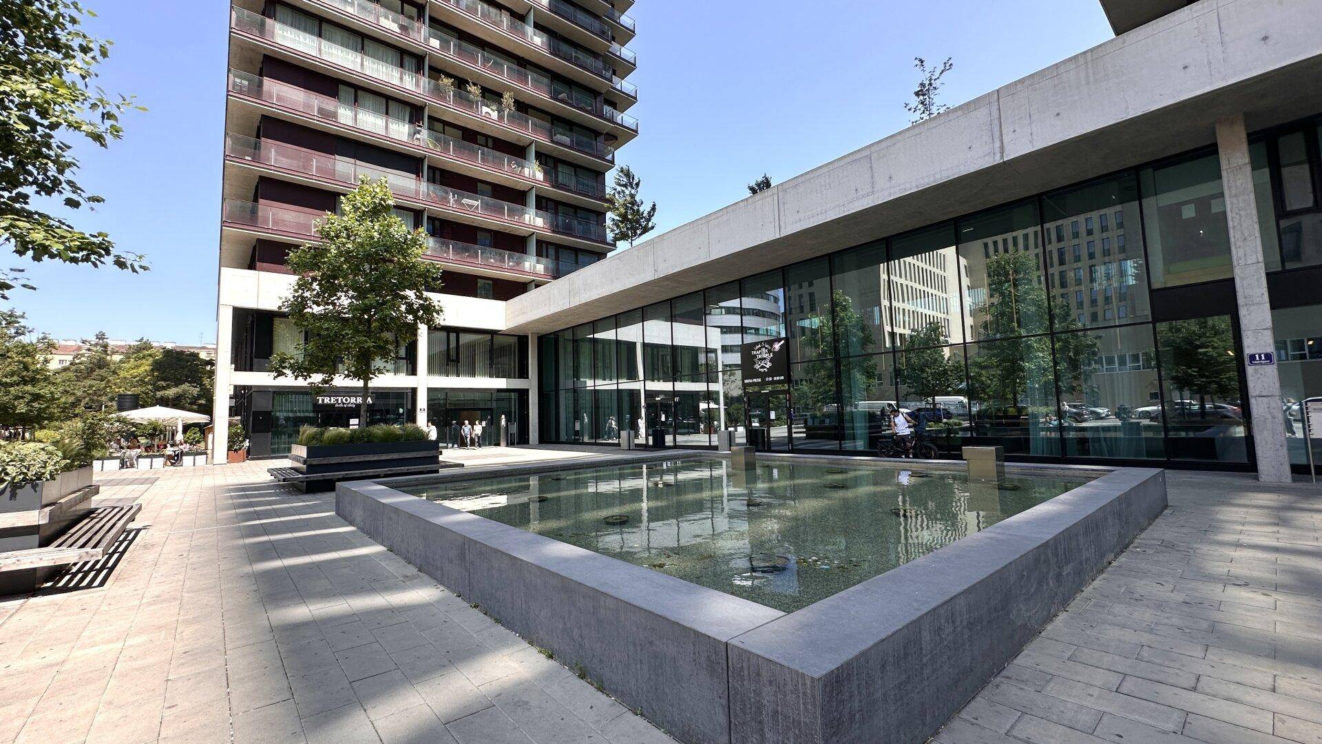 Moderne Gebäudefassade mit großen Glasflächen und einem dekorativen Wasserbecken im Außenbereich.