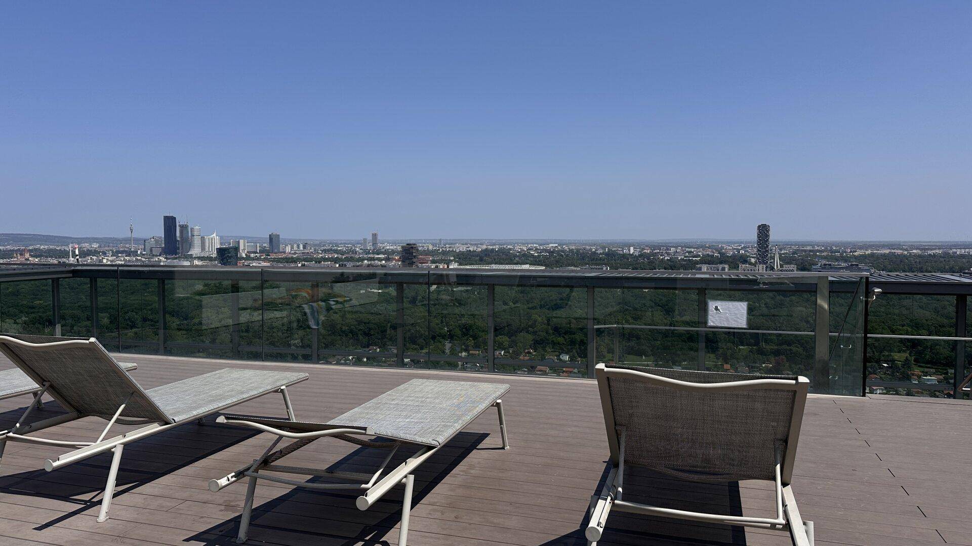 Dachterrasse mit Liegestühlen und weitem Panoramablick über die Stadt und die Umgebung.