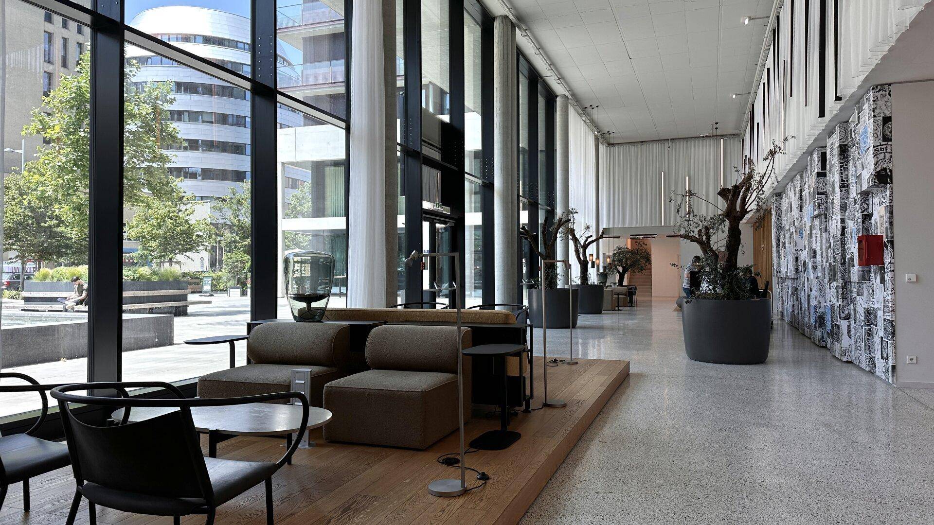 Geräumige, moderne Lobby mit großen Fenstern, bequemen Sitzgelegenheiten und viel Tageslicht.