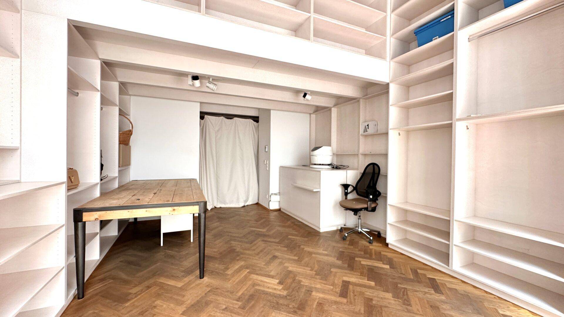 Geräumiger Loft-Bereich mit Regalsystemen, Holztisch und Arbeitsplatz.